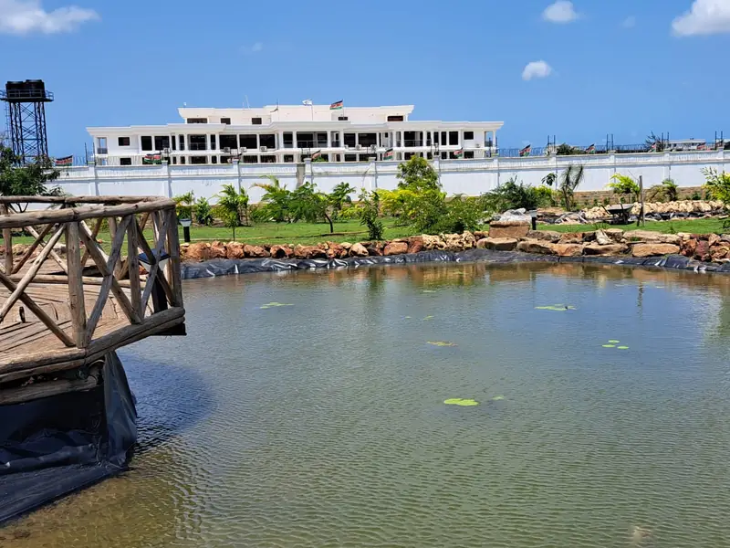 Large pond with a timber bridge in front of a white civic building, Kilifi park